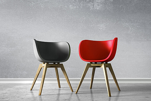 
                Roter und schwarzer Stuhl stehen nebeneinander auf grauem Boden
            