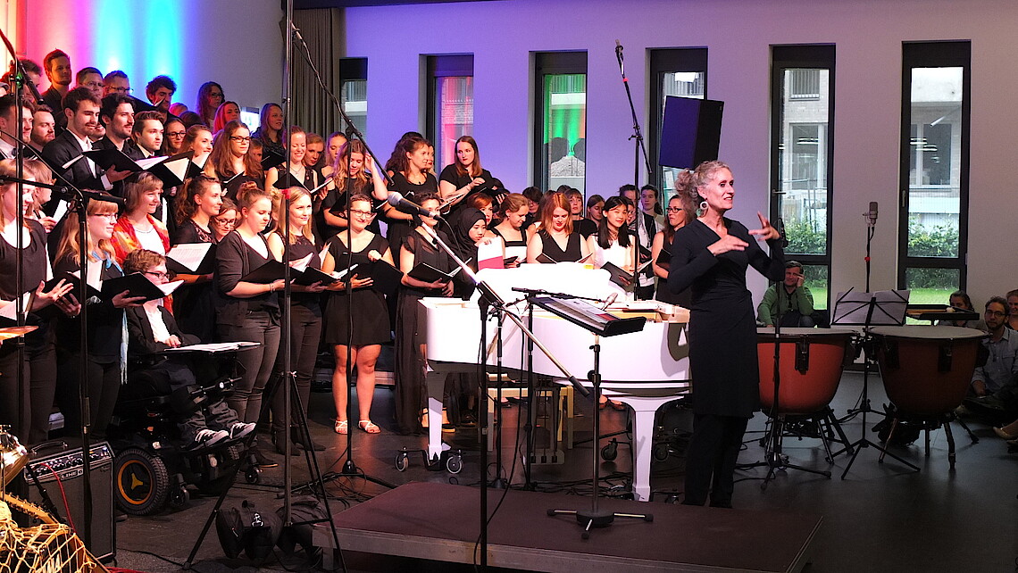 Chorleiterin Uschi Krosch steht vor dem Chor ans Publikum gerichtet 