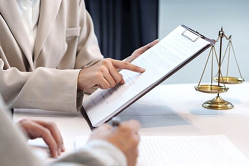 
                Finger auf Blatt Papier im Klemmbrett über einer Waage
            