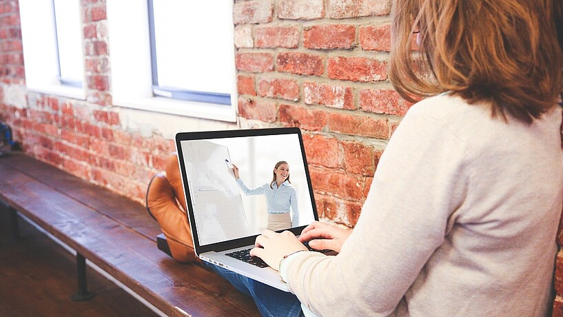 Innovative Konzepte zu hybriden Lernangeboten Eine Frau sitzt mit ausgestreckten Beinen auf einer Bank, vor sich auf den Beinen einen Laptop