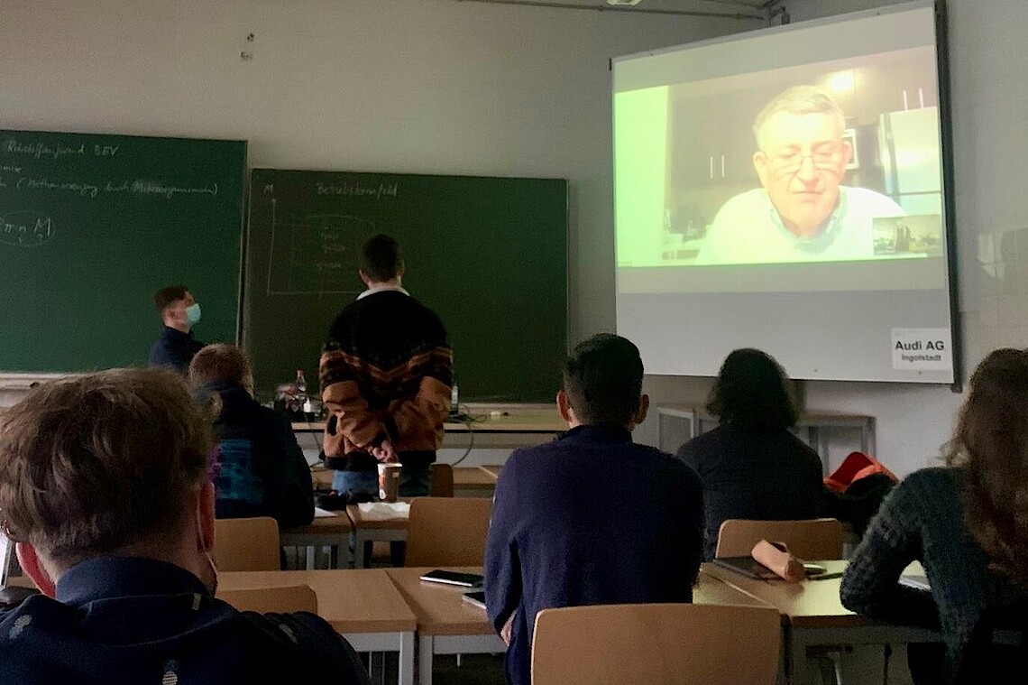 Seminarraum mit Leinwand und Studierenden, die einer Online-Vorlesung folgen
