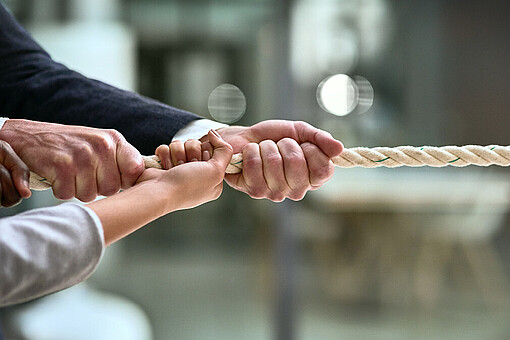 Krisenfest im Team: Mit psychischer Resilienz gesund und erfolgreich zusammenarbeiten
Vier Hände ziehen wie beim Tauziehen an einem Ende eines Seils.