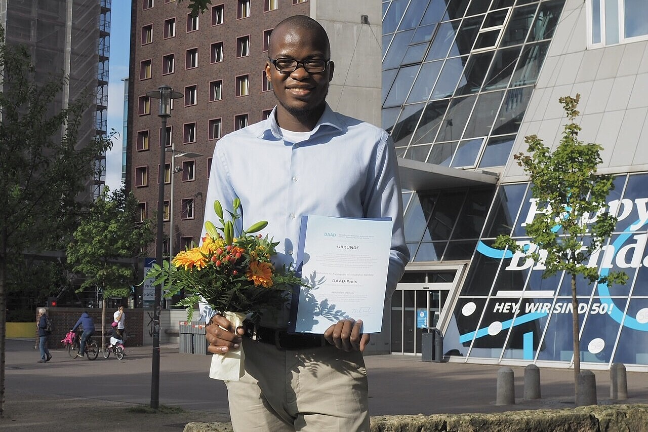 
                African student with prize certificate in front of university building
            