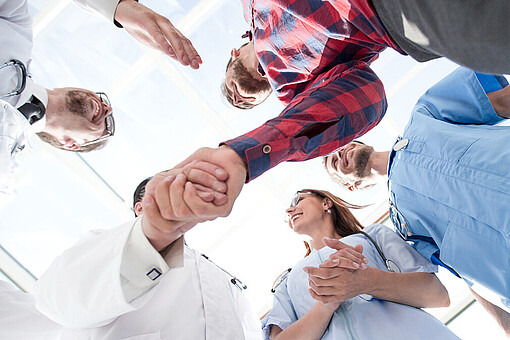 
                Pflegekräfte in Arbeitskleidung in Person in Straßenkleidung reichen sich die Hände
            