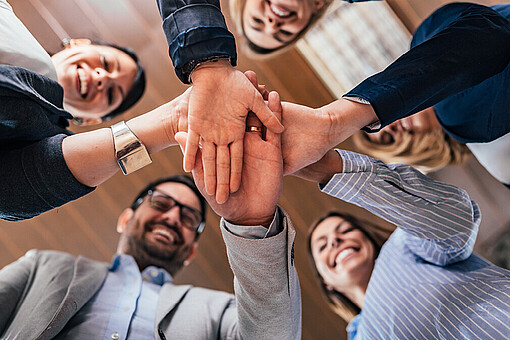 Kommunikative Führung zwischen Widerstand und Vertrauen
Es wird von unten nach oben auf fünf Personen geschaut, welche sich die Hände reichen.