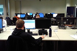 
                Das Bild zeigt den Raum in dem Studierende E-Assessment nutzen. Im Raum stehen mehrere Tischreihen mit Computern. Studierende sitzen an diesen PCs zum E-Assessment.
            