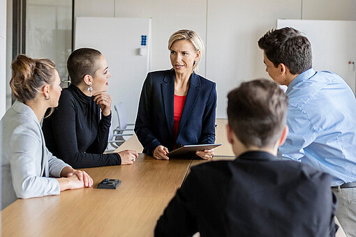 
                Fünf Personen sitzen an einem Tisch und reden miteinander.
            